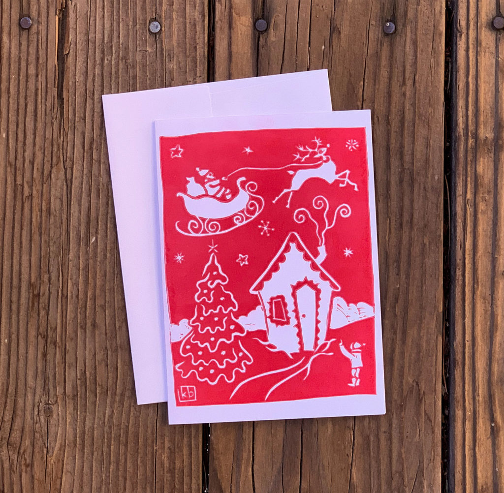 linocut notecard of santa in sleigh with reindeer in sky over playhouse and child pointing